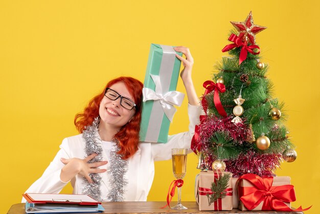 Ärztin der Vorderansicht, die mit Weihnachtsgeschenken auf gelbem Hintergrund sitzt