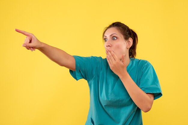 Ärztin der Vorderansicht im medizinischen Hemd, das etwas mit geschocktem Gesicht auf gelbem Hintergrund betrachtet