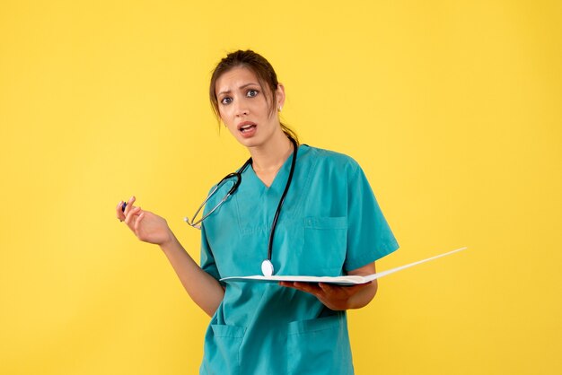 Ärztin der Vorderansicht im medizinischen Hemd, das Notizen auf gelbem Hintergrund hält