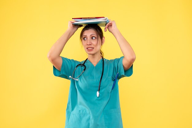Ärztin der Vorderansicht im medizinischen Hemd, das Notizen auf gelbem Hintergrund hält
