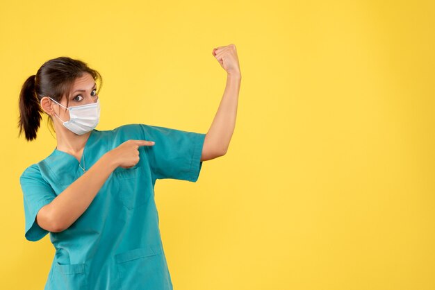 Ärztin der Vorderansicht im medizinischen Hemd und in der sterilen Maske, die auf gelbem Hintergrund biegt