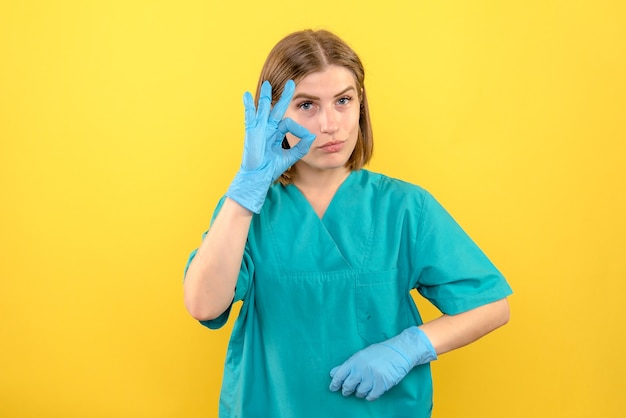 Ärztin der Vorderansicht mit blauen Handschuhen auf medizinischem Krankenhaus der Krankenschwester des gelben Bodens