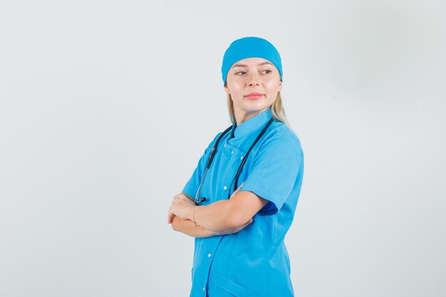 Ärztin, die Arme kreuzt, während sie in der blauen Uniform zurückblickt und hoffnungsvoll aussieht.