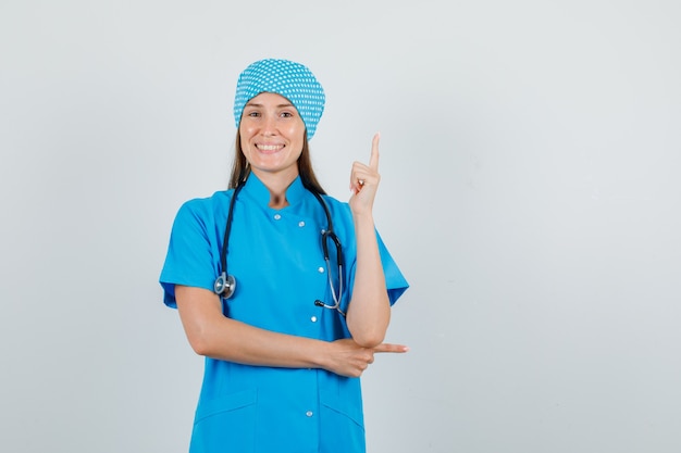 Ärztin, die Finger in blauer Uniform zeigt und fröhlich aussieht. Vorderansicht.