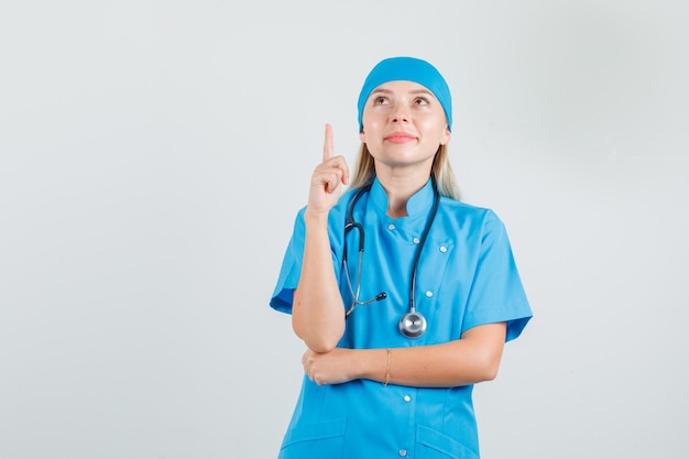 Ärztin, die Finger in blauer Uniform zeigt und hoffnungsvoll aussieht