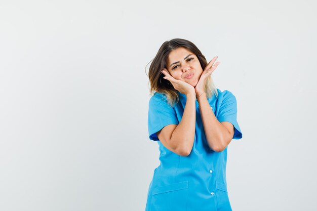Ärztin, die Gesicht auf ihren Händen in blauer Uniform polstert und hübsch aussieht