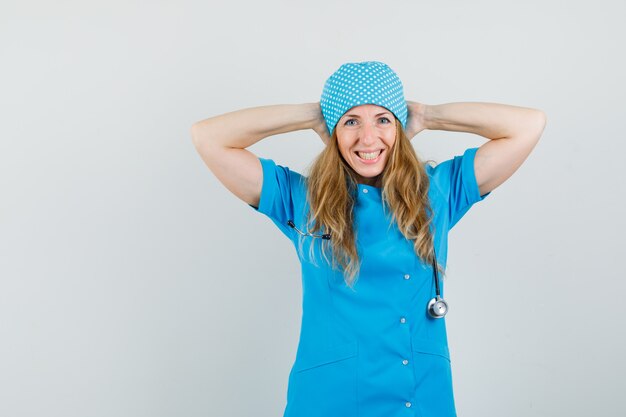 Ärztin, die Hände hinter Kopf in blauer Uniform hält und glücklich schaut.