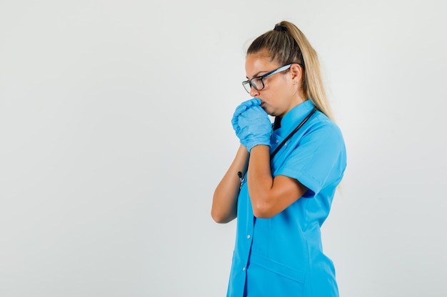 Ärztin, die Hände in der Gebetsgeste in der blauen Uniform fasst