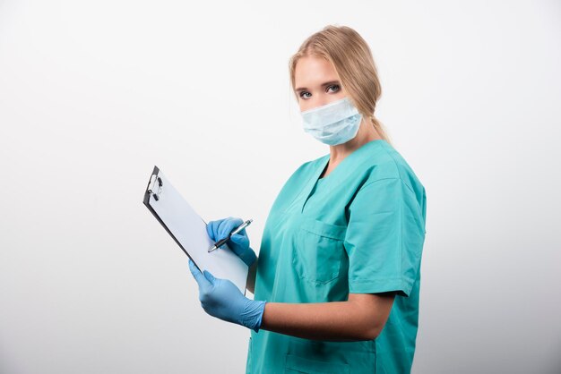 Ärztin, die in Zwischenablage schreibt und eine medizinische Maske trägt. Hochwertiges Foto