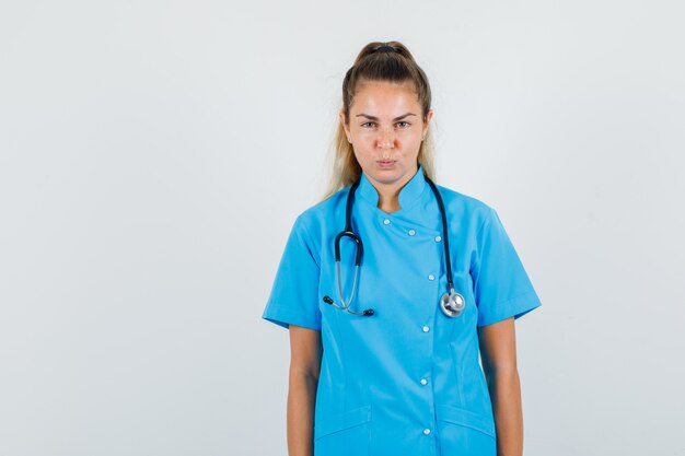 Ärztin, die Kamera in der blauen Uniform betrachtet und fokussiert schaut.