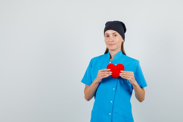 Ärztin, die rotes Herz hält und in der blauen Uniform, schwarzen Hut lächelt