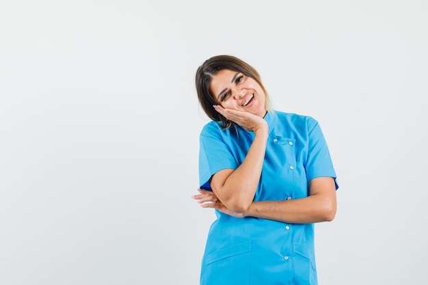 Ärztin, die sich in blauer Uniform auf die Handfläche stützt und optimistisch aussieht
