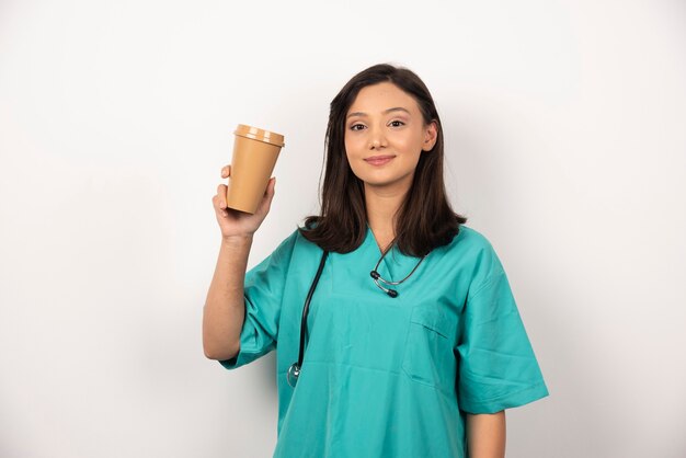 Ärztin, die Tasse Kaffee auf weißem Hintergrund zeigt. Hochwertiges Foto
