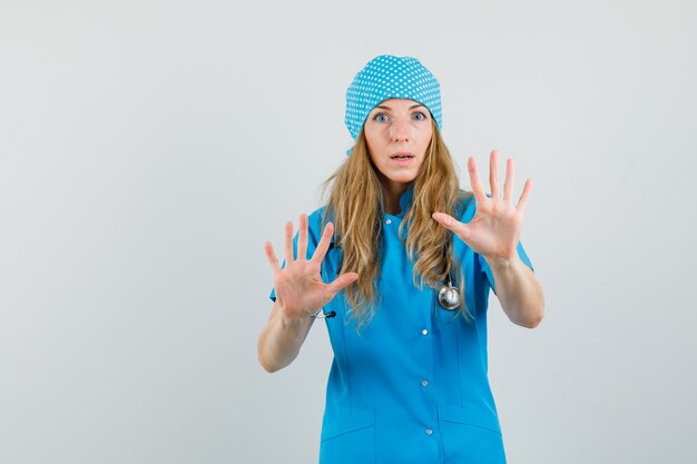 Ärztin, die vorbeugend Palmen in blauer Uniform zeigt und ängstlich aussieht.