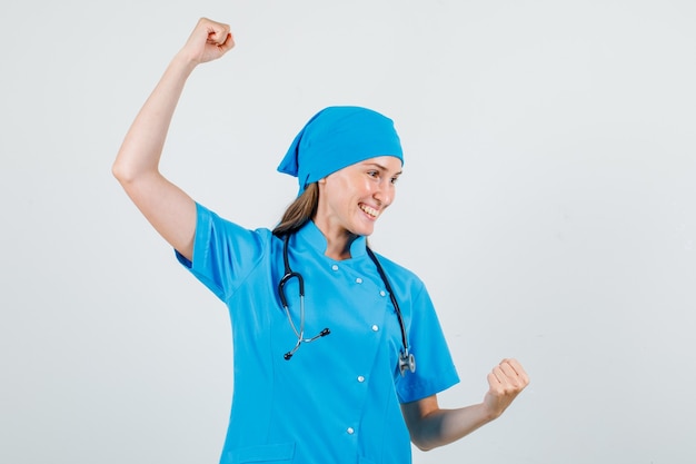 Ärztin feiert Sieg mit erhobenen Fäusten in blauer Uniform und sieht glücklich aus