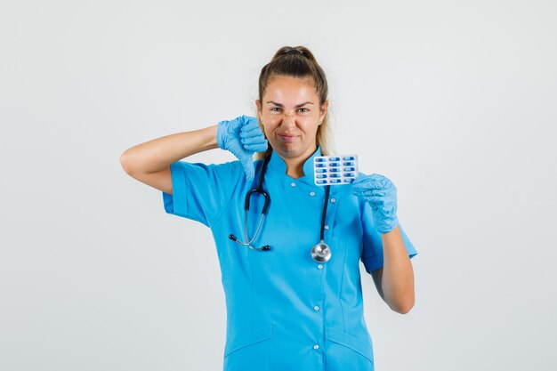 Ärztin hält Kapseln mit Daumen nach unten in blauer Uniform