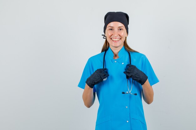 Ärztin Händchen haltend auf Stethoskop in Uniform, Handschuhe und froh aussehen