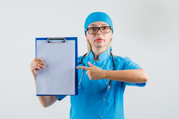 Ärztin in blauer Uniform, Brille zeigt Finger auf Zwischenablage