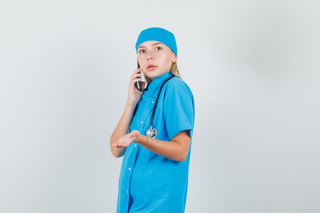 Ärztin in blauer Uniform, die auf Handy mit Handzeichen spricht und vorsichtig schaut.