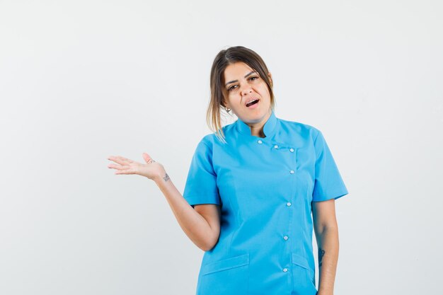 Ärztin in blauer Uniform, die etwas begrüßt oder zeigt und selbstbewusst aussieht