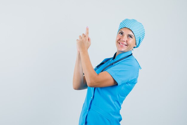 Ärztin in blauer Uniform, die Fingerpistolenzeichen macht und fröhlich schaut, Vorderansicht.