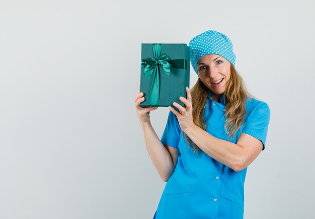 Ärztin in blauer Uniform, die Geschenkbox hält und fröhlich schaut