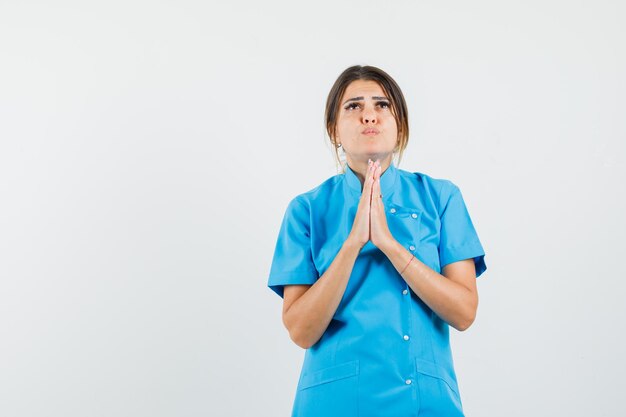 Ärztin in blauer Uniform, die Hände in betender Geste hält und hoffnungsvoll aussieht