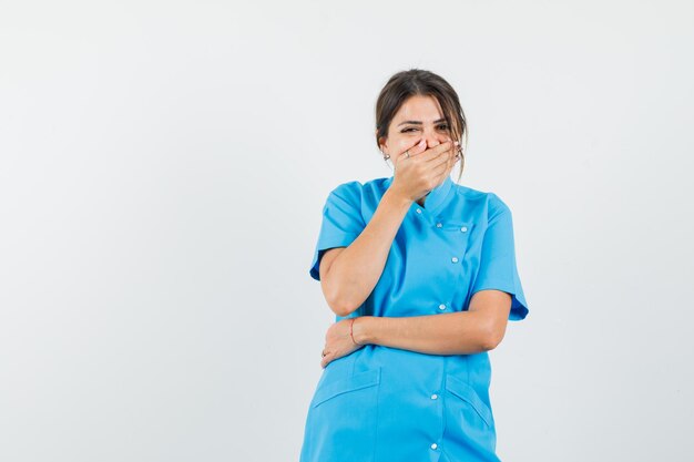 Ärztin in blauer Uniform, die Hand am Mund hält und glücklich aussieht looking
