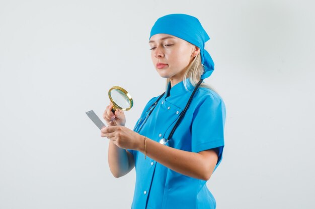Ärztin in blauer Uniform, die Lupe über Pillenpackung hält