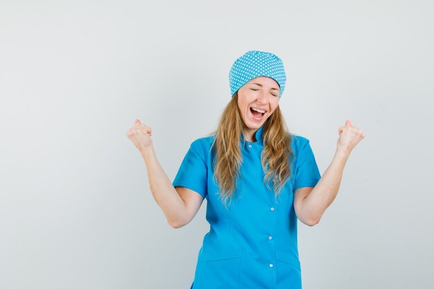 Ärztin in blauer Uniform, die Siegergeste zeigt und glücklich schaut