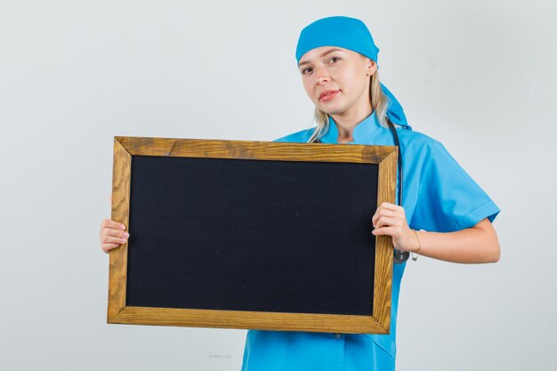 Ärztin in blauer Uniform, die Tafel hält und lächelt