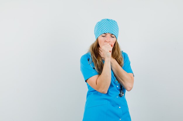 Ärztin in blauer Uniform, die unter Husten leidet und krank aussieht