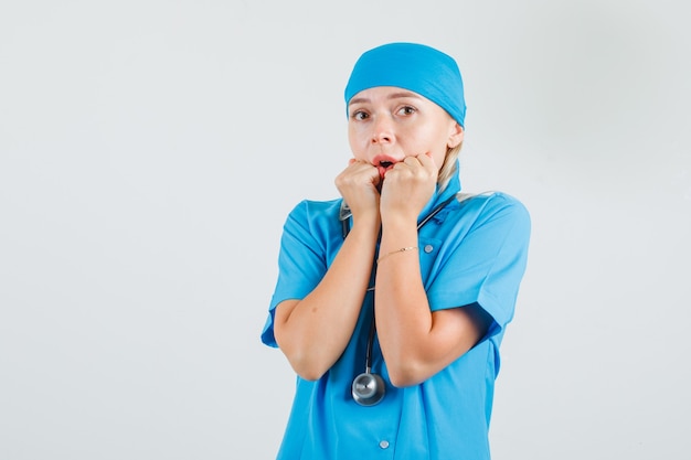 Ärztin in blauer Uniform hält Fäuste in der Nähe des Mundes und sieht ängstlich aus