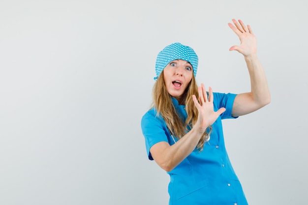 Ärztin in blauer Uniform hebt die Handflächen, um sich zu verteidigen, und sieht verängstigt aus