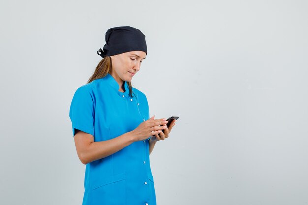 Ärztin in blauer Uniform, schwarzer Hut mit Smartphone und Blick beschäftigt