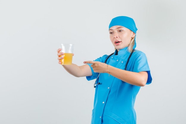 Ärztin in blauer Uniform zeigt Finger auf Fruchtsaft