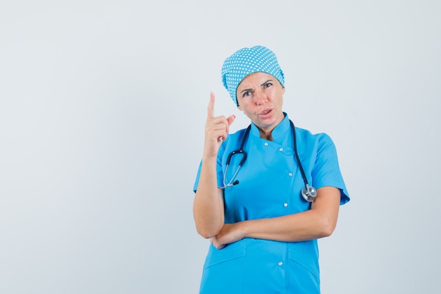 Ärztin in blauer Uniformwarnung mit Finger und Blick wütend, Vorderansicht.