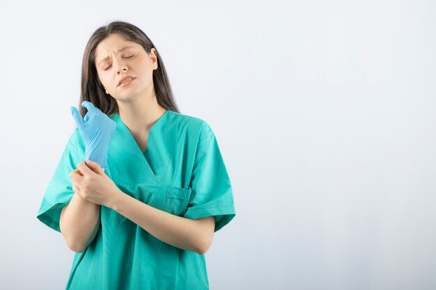 Ärztin in den medizinischen Handschuhen, die Hände auf Weiß zeigen.