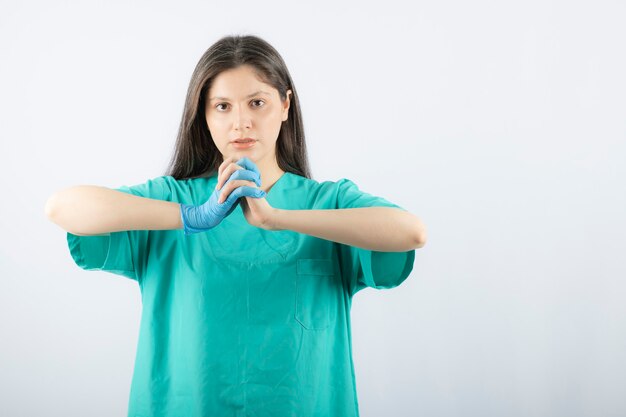 Ärztin in den medizinischen Handschuhen, die Hände auf Weiß zeigen.