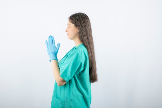 Ärztin in den medizinischen Handschuhen, die Hände auf Weiß zeigen.