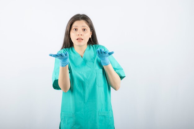 Ärztin in den medizinischen Handschuhen, die Hände auf Weiß zeigen.