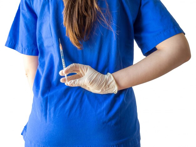 Ärztin in einer blauen medizinischen Uniform mit sterilisierten Handschuhen, die eine Spritze hinter ihrem Rücken halten