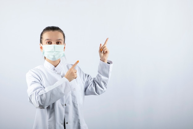Ärztin in weißer Uniform, die eine medizinische Maske trägt und wegzeigt