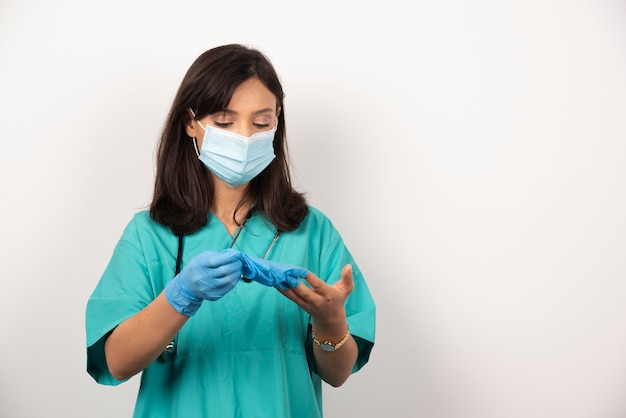 Ärztin mit medizinischer Maske, die Paar Handschuhe auf weißem Hintergrund betrachtet.