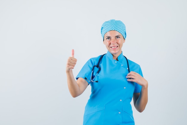 Ärztin zeigt Daumen oben in blauer Uniform und sieht fröhlich aus, Vorderansicht.