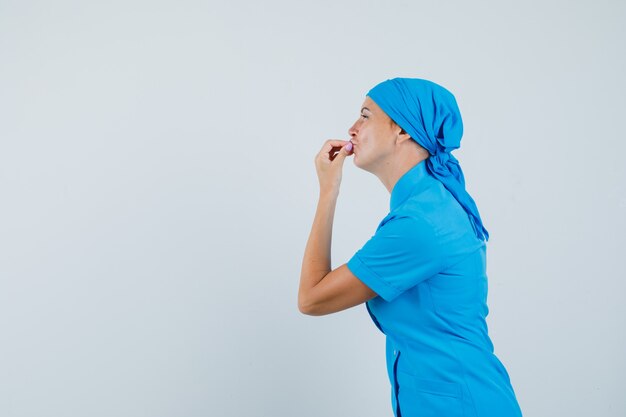 Ärztin zeigt köstliche Geste in blauer Uniform und sieht entzückt aus.