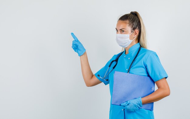 Ärztin zeigt zur Seite, während sie die Zwischenablage in blauer Uniform hält