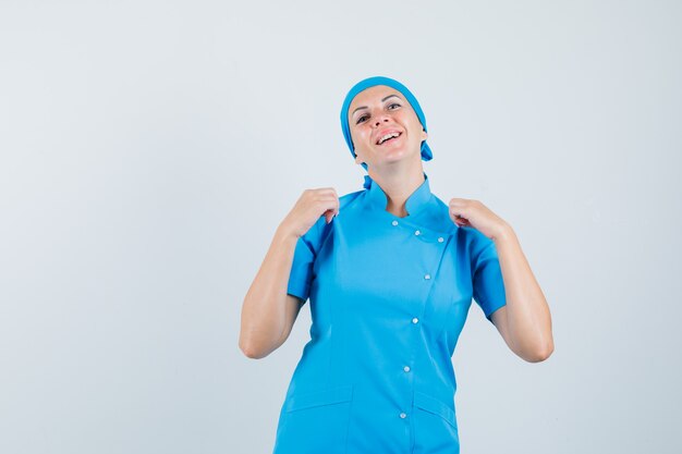 Ärztin zieht ihre Uniform in blauer Uniform und sieht stolz aus, Vorderansicht.