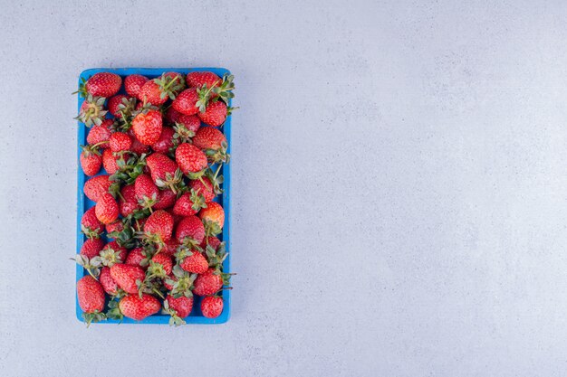 Saftige Erdbeeren gehäuft in ein blaues Tablett auf Marmorhintergrund. Foto in hoher Qualität