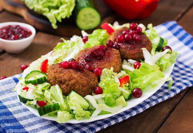 Saftige Fleischkoteletts mit Preiselbeersoße und Salat auf einem Holztisch in einer rustikalen Art.
